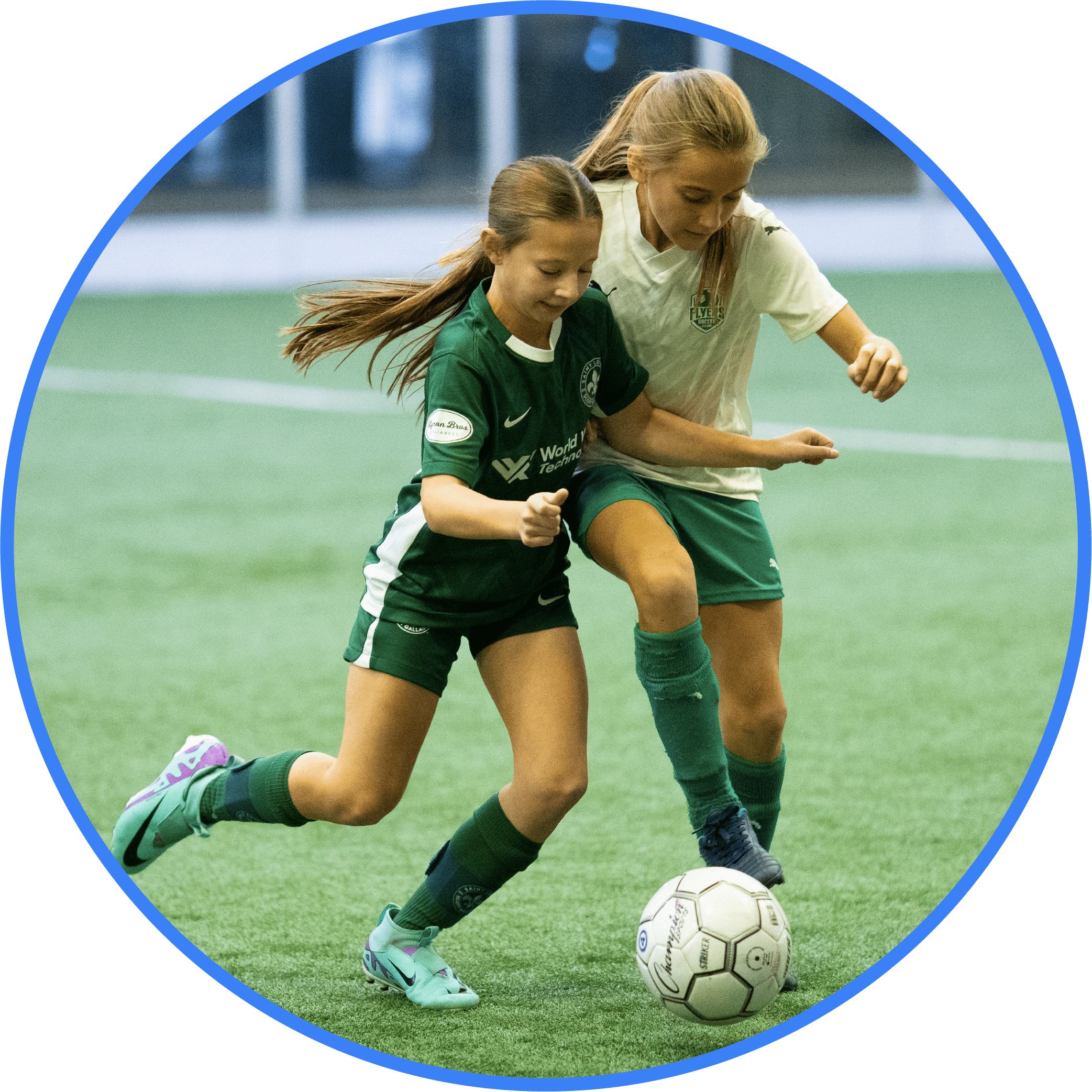 Two girls wearing green soccer uniforms compete for control of a soccer ball on an indoor field, showcasing the excitement and skill found in Vetta Sports youth soccer league registration. Both are focused, with one trying to block the other from advancing.
